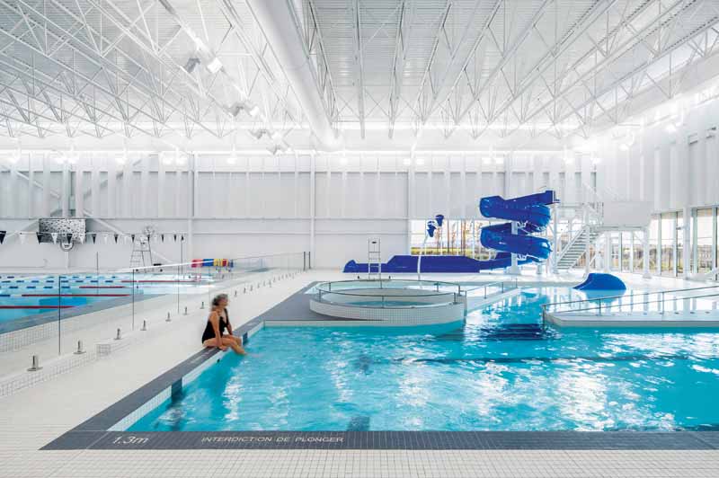 A woman sits on the edge of a swimming pool in an aquatic center. 