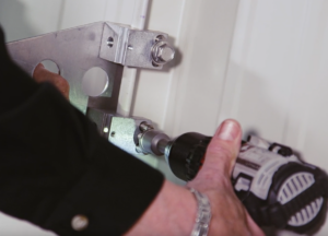 Courtesy AceClamp A worker screws in a bar snow guard for a standing seam metal roof.