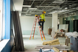 A worker climbs as ladder while working on a metal ceiling.