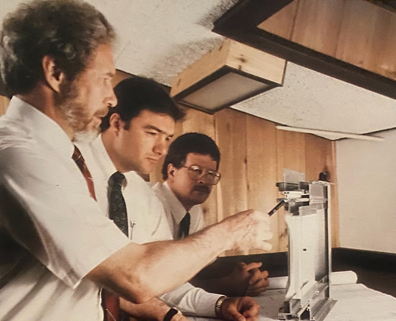 Photo courtesy Exterior Technologies Inc. (EXTECH) Three men in collared shirts and ties look at a window system mock-up