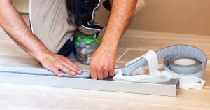 Construction worker applying sealing tape meticulously to a metal profile for drywall, ensuring effective insulation and preventing potential cracks in the wall during renovation
