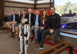A team of people gathers around a humanoid robot. A pilot project for these robots will be held at SSE Steel Fabrication in Louisiana. 