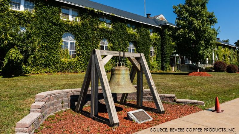 Exterior view of Revere Copper Products’ campus in Rome, N.Y., showing an ivy-covered building, landscaped grounds, and a bell display.