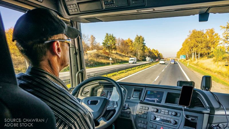 Interior view of a truck cab with a driver behind the wheel and a highway visible through the windshield.