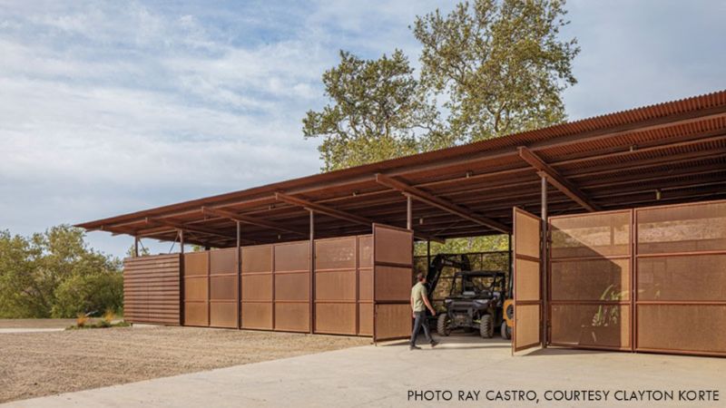 Alma Rosa Vineyard barn with weathering steel framing and perforated metal cladding, with large doors open to stored farm equipment.