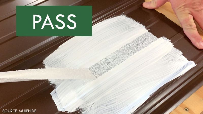 Polyester fabric pulled from white roof coating that remains adhered to a brown metal roof panel during an adhesion test.