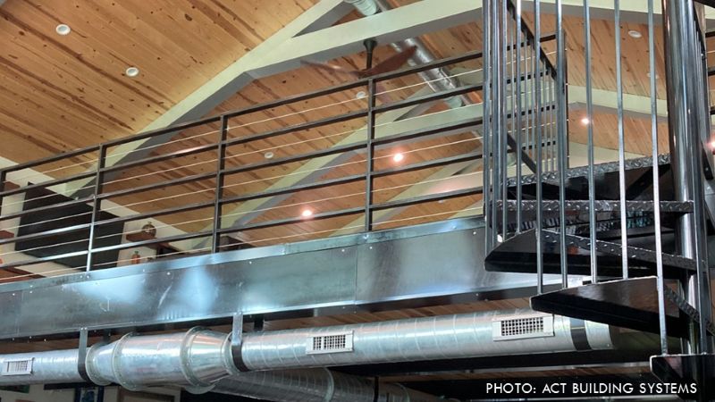 Interior view of a steel-framed mezzanine with metal railings, a spiral staircase, exposed ductwork, and a wood-paneled ceiling.